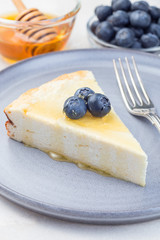 Piece of cheese casserole or cheesecake, garnished with blueberry and honey, on gray plate, vertical