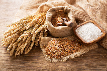wheat ears, grains and bowl of flour on a wooden table