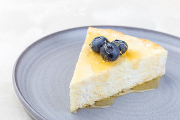 Piece of cheese casserole or cheesecake, garnished with blueberry and honey, on gray plate, horizontal, copy space