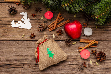 Spirit Christmas background. Gift in sack, New Year tree, apple, candles, spices, deer, cones. Nature decorations, vintage wooden boards