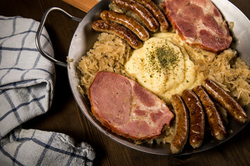 Sauerkraut Pfanne mit Nürnberger Rostbratwürste, Kassler Nacken und Kartoffelpüree auf Holz Tisch