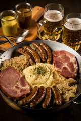 Sauerkraut Pfanne mit Nürnberger Rostbratwürste, Kassler Nacken,  Kartoffelpüree Senf und Bier auf Holz Tisch