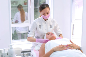 Cosmetologist in gloves washes cleans client's woman face wiping with napkins. Beautician making massaging beauty facial skincare procedure to patient in clinic. Beauty industry concept.