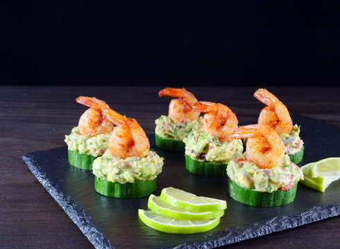 Canape with cucumber, avocado salad and shrimp on black slate platter against dark background