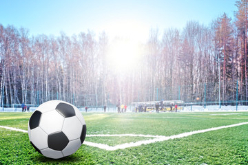 Traditional football ball in corner of soccer pitch field with white snow at winter against football team training blur background. Stadium in forest park. Сold season outdoor sport activity concept © vaalaa