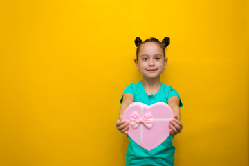 happy little girl with tails standing isolated over yellow background holding shopping pink bag. smiles thoughtfully