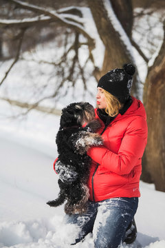 Portrait of happy woman playing with her cute small black pet miniature zwerg schnauzer dog outdoor in fresh white snow with. Kissing and hugging favorit animal. Vertical color photography.