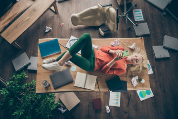 High angle view photo of corporate messy atmosphere careless blond business lady lying table don't mind cluttered office disorder texting telephone wear casual outfit indoors
