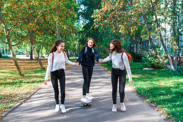 Fototapeta premium Girls teenage schoolgirls ride a skateboard after school, happy smiling, emotions of joy, delight and fun, warm sweaters in autumn on street in city. Best friends girlfriends.