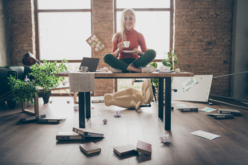 Full body photo of happy trader woman sit on table crossed legs feel carefree careless rest relax hold white coffee cup in messy office loft