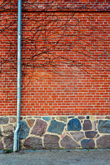 Downpipe on a red brick wall with natural stone foundation.