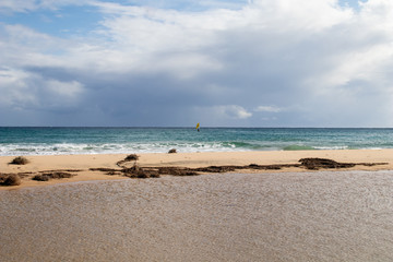 Mediterranean sea coast with beach, sun and cloudy sky. Sea and vacation in winter, yellow beach and waves that reach the shoreline. Blue and emerald green water