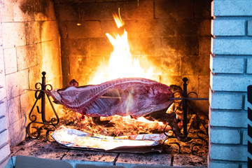Sardinian pig on a spit, cooking on the grill and near the living flame of a fire. spit roast pork, barbecue and meat cooked over a high heat. Italian regional cuisine. grilled pork and high flame