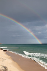 Sardinian coast, rough sea and cloudy sky after the rain with a rainbow that is born on the sea. Rainbow over the sea after a heavy rain. Abnormal rains and storms on the Mediterranean sea