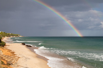 Sardinian coast, rough sea and cloudy sky after the rain with a rainbow that is born on the sea. Rainbow over the sea after a heavy rain. Abnormal rains and storms on the Mediterranean sea