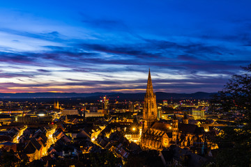 Fototapeta na wymiar Germany, Big city lights of freiburg im breisgau skyline and cityscape illuminated by night in magical twilight after sunset, aerial view from above the roofs