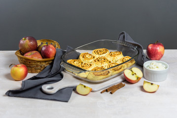 Freshly baked cinnabon buns in a shape stand on a white wooden table. Around are apples, showing what's in the filling. Above is a great place for text or recipe.