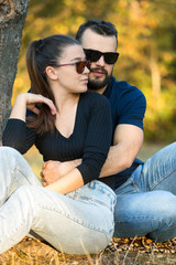 Portrait of a man and a woman in sunglasses in the woods. Young stylish couple on the background of nature. Warm autumn evening in the forest.