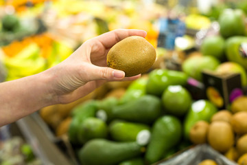 Woman's hand choosing kiwi in the market. Concept of healthy food, bio, vegetarian, diet.