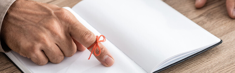 panoramic shot of senior man with red bow on finger as reminder near notebook