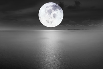 Aerial view Dramatic atmosphere of peaceful black and white image of the ocean with beautiful bright full moon and dark sky background. Image of moon furnished by NASA.