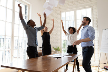 Overjoyed young multiracial team throwing papers in air.