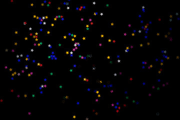 Multi-colored stars on a black background. Festive background of colorful confetti stars on a black background.