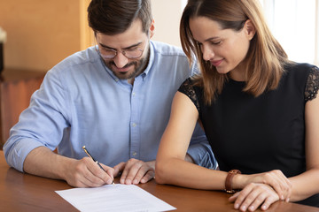 Fototapeta premium Pleasant young woman watching smiling husband signing contract.