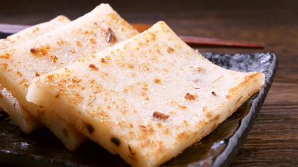 Pouring black soy sauce on ready-to-eat delicious turnip cake, Chinese traditional local dish radish cake in restaurant, close up, copy space.