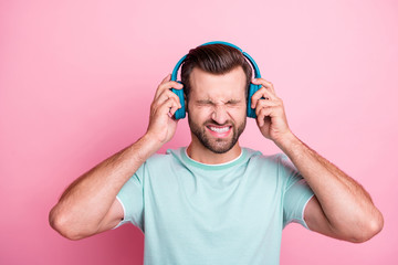 Frustrated man feeling anger cant suffer loud stereo music from his modern blue wireless headset have headache close eyes wear casual style clothing isolated over pink color background