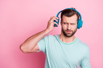 What is it. Frustarted music lover man disdlike his playlist song he listen from blue modern headset feel confused expression wear casual style clothes isolated over pink color background