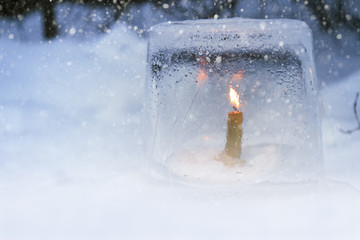 Winter lantern made of ice, burning candle inside, in snowfall.