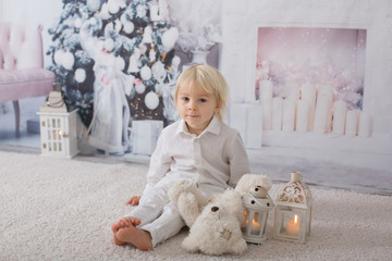 Beautiful blonde toddler boy, dressed in white in decorated white room for Christmas