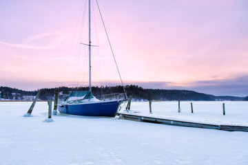 Sailboat is stuck in ice in the winter, Kaarina, Finland. Beautiful sunset in the background.