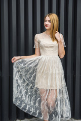 Young woman in evening dress posing on city street, dark wall background