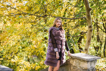 Fashion dresses woman in fur coat and dress posing in autumn park