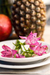 Tropical paradise heaven asian thai pink iris flower on white plate, pineapple, pomegranate on wooden tray in spa resort, restaurant. Holidays rest at sea. Food of gods. Table setting decoration