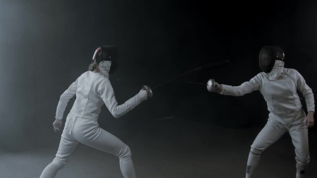 Fencing training in the dark studio - two women having a duel