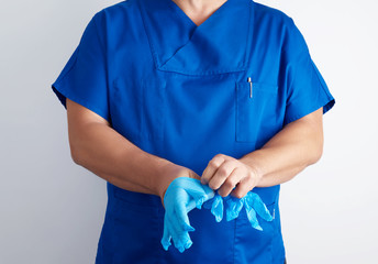 male doctor in blue uniform puts on his hands white sterile latex gloves before surgery