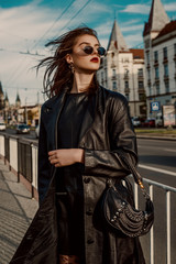 Outdoor fashion portrait of young elegant brunette woman wearing trendy sunglasses, long black...