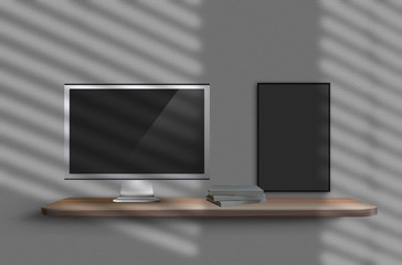 Monitor and three books on shelf suspended from gray wall with shadows from window on it, picture blank hanging nearby. Mockup. Copy space, close-up.