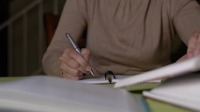 Woman doing her assignment by referring to books and writing on notepad.