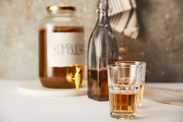 selective focus of jar with kombucha near glasses and bottle on textured grey background with striped napkin