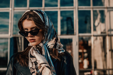 Outdoor close up fashion portrait of young elegant model, woman wearing trendy headscarf, black cat eye sunglasses, posing in street of city. Copy, empty space for text - Powered by Adobe