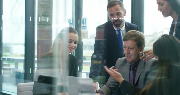 4K Business execs in a meeting, looking at laptop & brainstorming