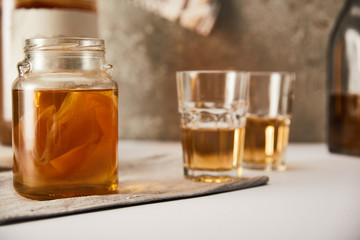 selective focus of jar with kombucha near glasses on textured grey background