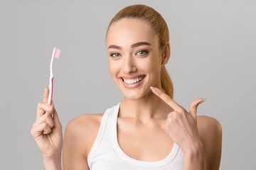 Woman with toothbrush pointing at her perfect teeth