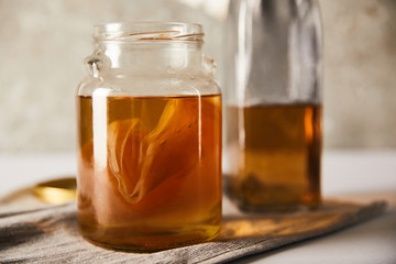 selective focus of jar with kombucha near bottle on grey napkin