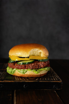 Bitten vegetarian burger on wooden board on dark background