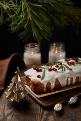 traditional Christmas cake with cranberry near pine, baubles and candles on wooden table